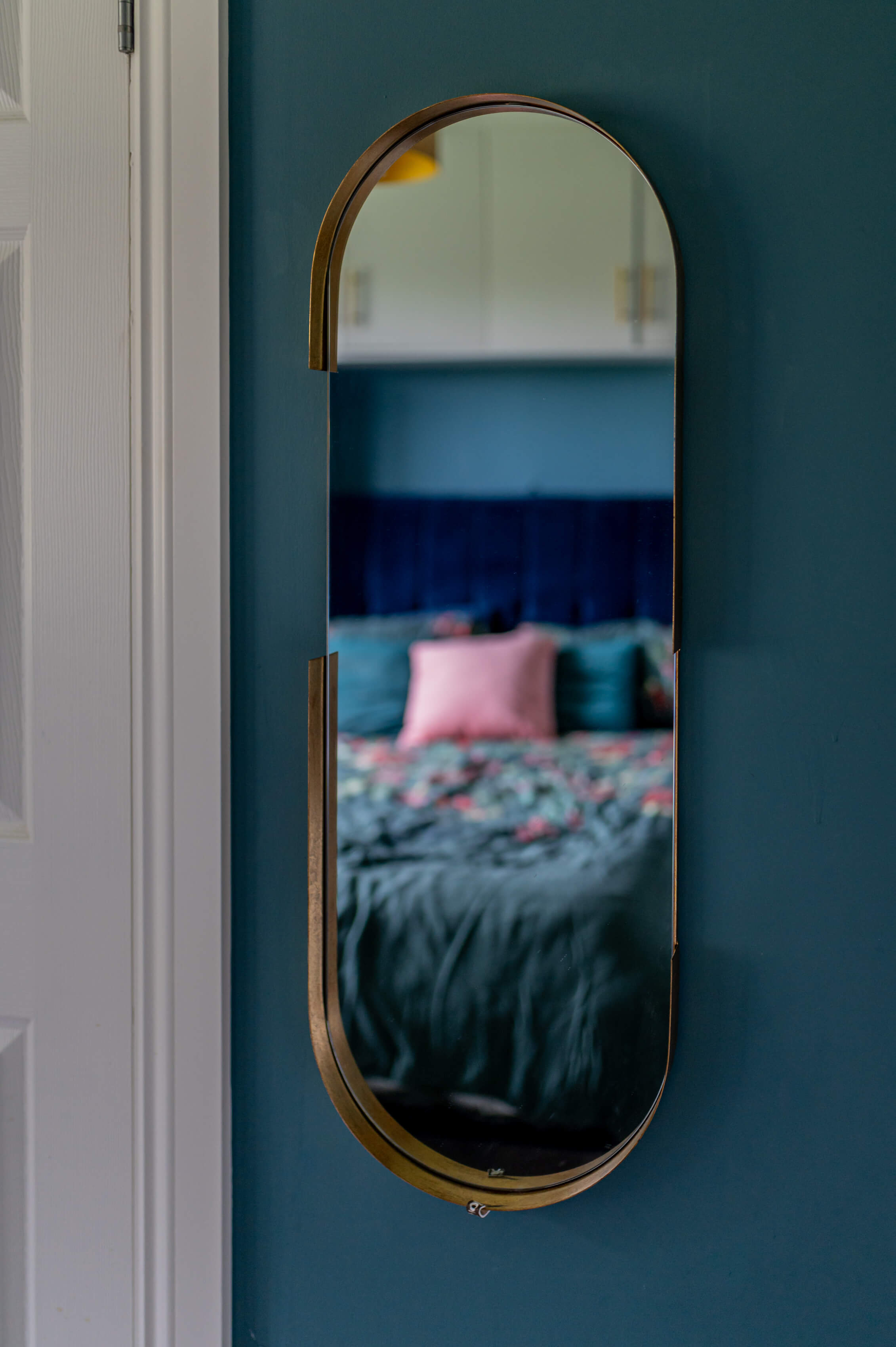 a gold, oval, long mirror in a bedroom on a green teal wall.